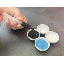 Hand füllt mit Spritze schwarze Farbe in einen Farbmischteller