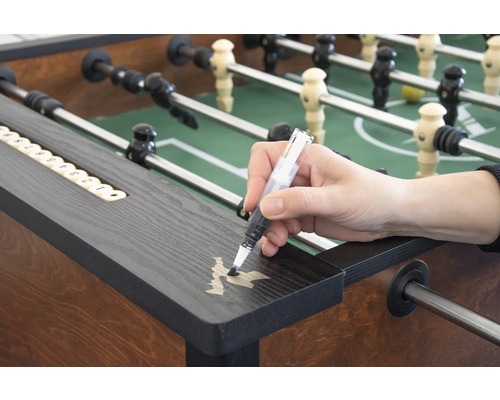 Eine Person retuschiert Kratzer auf einem Tischfußballtisch mit einem Lackstift.
