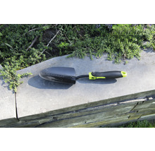 Gartenschaufel auf einer Mauer mit Pflanzen im Hintergrund