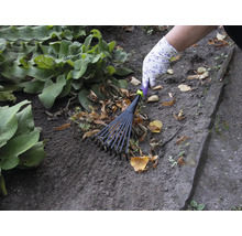 Eine Person rechen Laub mit einem Fächerbesen im Garten.