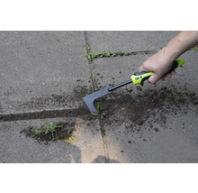 Eine Person entfernt Unkraut mit einem Fugenkratzer auf einer gepflasterten Fläche.