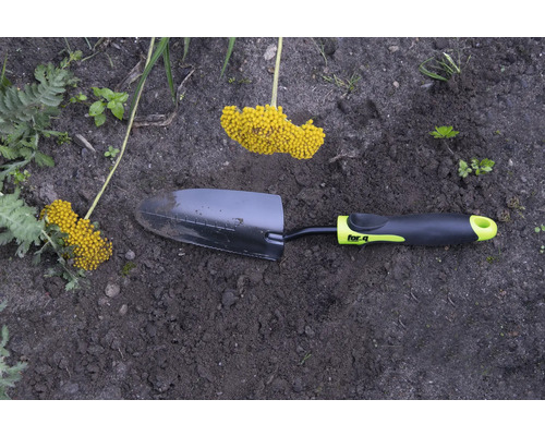 Gartenschaufel mit gelbem Blütenstand im Gartenbeet