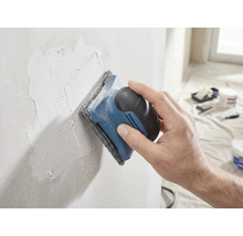 Eine Hand schleift eine verspachtelte Wand mit einem Handschleifer und Schleifvlies glatt.