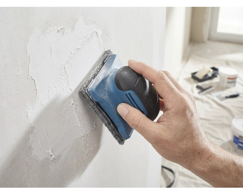 Eine Hand schleift eine verspachtelte Wand mit einem Handschleifer und Schleifvlies glatt.