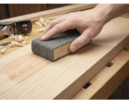 Hand schleift ein Holzbrett mit einem Schleifvlies auf einem Schleifklotz.