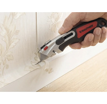 Hand mit Rautner Cuttermesser beim präzisen Abschneiden von Tapete mit Blumenmuster an einer Fußleiste.