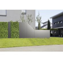 Moderner Sichtschutz aus grauen Paneelen und einer künstlichen Hecke auf einer Rasenfläche vor einem Wohnhaus.