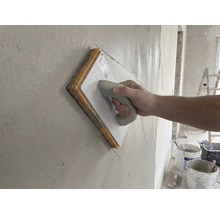 Hand führt ein Schwammbrett über eine frisch verputzte Wand.
