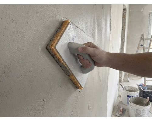 Hand führt ein Schwammbrett über eine frisch verputzte Wand.
