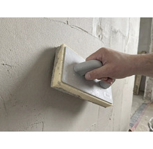 Hand führt ein Schwammbrett 28 mal 14 Zentimeter zum Glätten von frischem Putz über eine Wand.