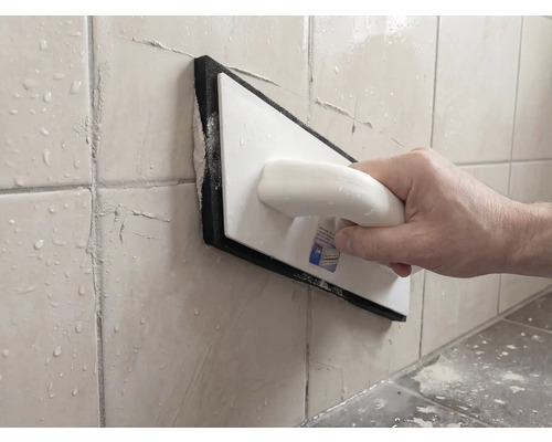 Person verfugt Wandfliesen mit einem Fugenbrett aus Kunststoff und Moosgummi.