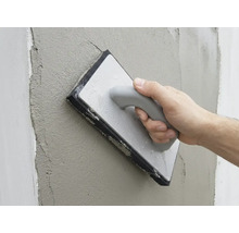 Hand glättet frischen Putz an einer Wand mit einem Reibebrett mit Schwammbelag.