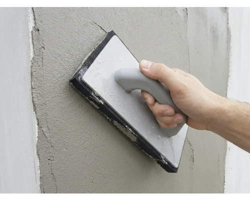 Hand glättet frischen Putz an einer Wand mit einem Reibebrett mit Schwammbelag.