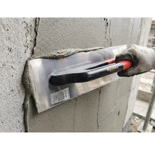 Anwendung einer Maurerlob Glättkelle beim Verputzen einer Betonwand mit Mörtel durch eine Person mit Arbeitshandschuh.