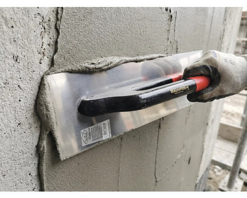 Anwendung einer Maurerlob Glättkelle beim Verputzen einer Betonwand mit Mörtel durch eine Person mit Arbeitshandschuh.