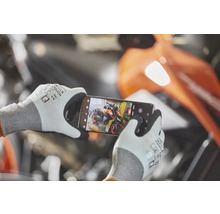 Eine Person trägt Arbeitshandschuhe mit Touch-Funktion und fotografiert ein Motorrad mit einem Smartphone in einer Werkstatt.