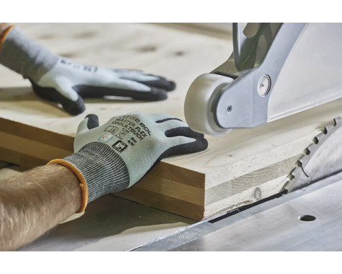 Hände in Arbeitshandschuhen führen ein Holzbrett an einer Tischkreissäge zur präzisen Holzbearbeitung.