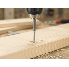 Akkuschrauber dreht eine Holzschraube mit einem Bit in ein helles Holzbrett, umgeben von Holzspänen.