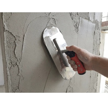 Glättekelle trägt grauen Putz auf eine Wand auf.