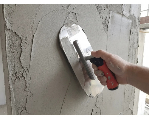 Glättekelle trägt grauen Putz auf eine Wand auf.
