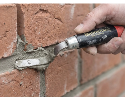Eine Person nutzt eine Maurerlob Fugenkelle zum Verfugen von roten Ziegelsteinen mit Mörtel.