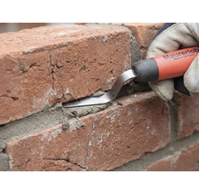 Eine Maurerlob Fugenkelle wird verwendet, um Mörtel in die Fuge zwischen zwei roten Ziegelsteinen zu drücken.