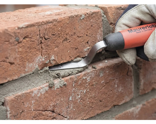 Eine Maurerlob Fugenkelle wird verwendet, um Mörtel in die Fuge zwischen zwei roten Ziegelsteinen zu drücken.