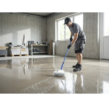 Ein Mann entlüftet eine frisch gegossene Bodenausgleichsmasse mit einer Stachelwalze auf einer Teleskopstange in einem hellen Raum.