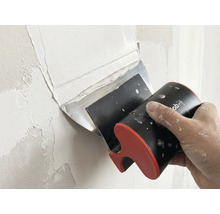 Hand trägt mit einem Flächenspachtel Spachtelmasse auf eine Wand auf.