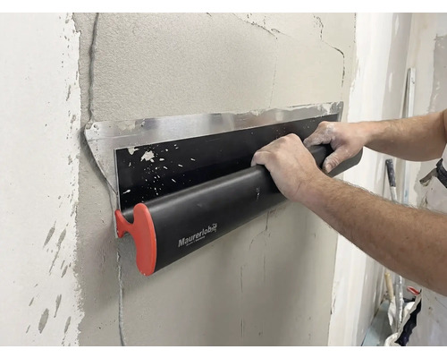 Eine Person verwendet eine Maurerlob Flächenspachtel, um feuchten Putz auf einer Wand glattzustreichen.