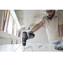 Person verwendet einen Bosch Akku-Schlagbohrschrauber zum Bohren in weiße Fliesen auf einer Baustelle.