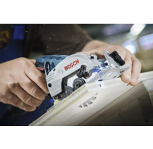 Eine Person schneidet mit einer Bosch Kreissäge ein Holzbrett, wobei Sägespäne entstehen.