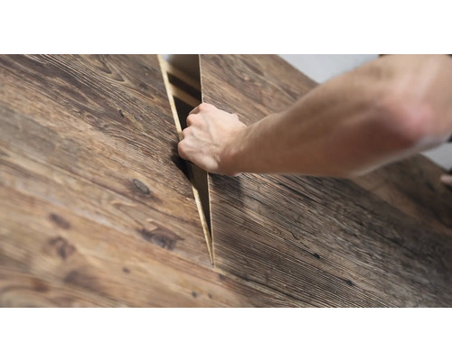 Eine Hand hebt ein strukturiertes Holzpaneel mit rustikaler Optik an.