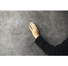 Eine Hand berührt eine strukturierte Wandverkleidung in Steinoptik.