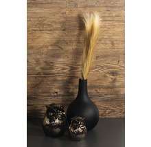Schwarze Vase mit Pampasgras neben zwei Eulenfiguren vor einer Holzwand.