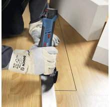 Person mit Schutzhandschuhen schneidet mit einem Bosch Professional Akku-Multicutter eine gerade Linie in einen Holzboden.