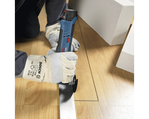 Person mit Schutzhandschuhen schneidet mit einem Bosch Professional Akku-Multicutter eine gerade Linie in einen Holzboden.