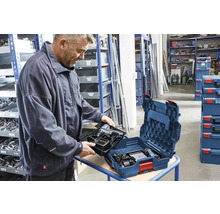 Ein Mann setzt eine Einlage mit Bosch Akku-Bohrschrauber und Ladegerät in eine Bosch L-BOXX Werkzeugkiste in einer organisierten Werkstatt ein.