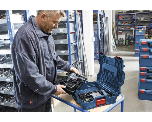 Ein Mann setzt eine Einlage mit Bosch Akku-Bohrschrauber und Ladegerät in eine Bosch L-BOXX Werkzeugkiste in einer organisierten Werkstatt ein.