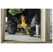 Handwerker nutzt eine batteriebetriebene DeWalt Säbelsäge zum Schneiden eines Kunststoffrohrs neben Holzständerwerk auf einer hellen Baustelle.