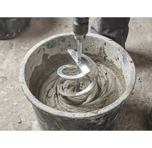 Ein Wendelrührer rührt grauen Mörtel in einem schwarzen Baueimer an.