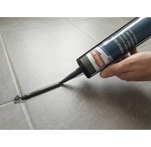 Modulan 600 Universal-Silikon wird mit einer Kartusche in eine Fliesenfuge auf grauen Bodenfliesen aufgetragen.