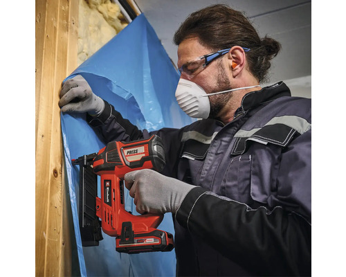 Handwerker mit Schutzausrüstung befestigt eine Dampfsperrfolie an einem Holzständer mit einem Einhell Akku-Nagler.