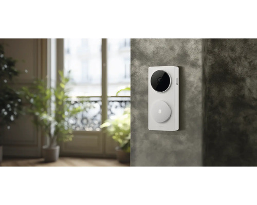 Weiße Video-Türklingel mit schwarzer Kamera und runder Klingeltaste, montiert an einer strukturierten Wand.