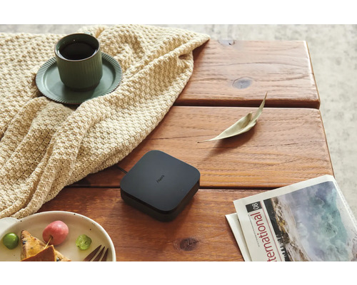 Aqara Smart Home Hub M2 auf einem Holztisch neben einer Tasse Kaffee auf einer Strickdecke, einem Teller mit Obst und einer Zeitschrift.