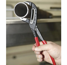 Eine Hand hält eine Virax Wasserpumpenzange mit roten Griffen, die ein Metallrohr umschließt.