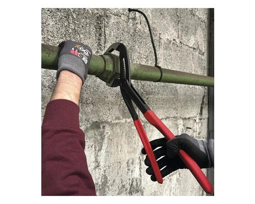 Wasserpumpenzange mit roten Griffen greift ein Metallrohr an einer Wand während einer Sanitärinstallation.
