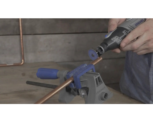 Mit einem Dremel Multifunktionswerkzeug und einer Trennscheibe wird ein Kupferrohr geschnitten, das in einem Schraubstock eingespannt ist.