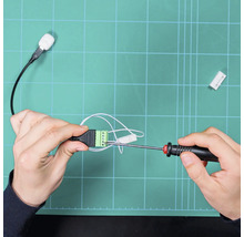 Hände befestigen Kabel mit einem Schraubendreher an einem grünen Klemmenblock.