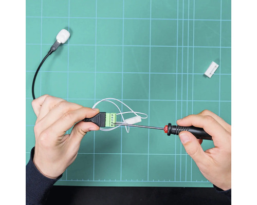 Hände befestigen Kabel mit einem Schraubendreher an einem grünen Klemmenblock.